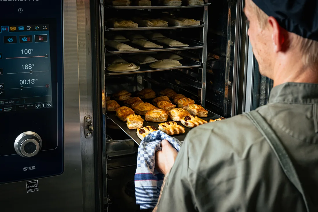 Chef haalt een bakplaat met versgebakken broodjes uit de oven
